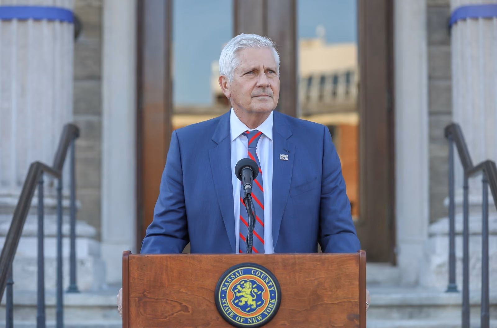 Bruce Blakeman speaking at a podium with the Nassau County seal.