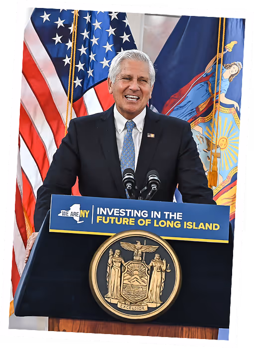 Bruce Blakeman speaking at a podium with American and New York flags.